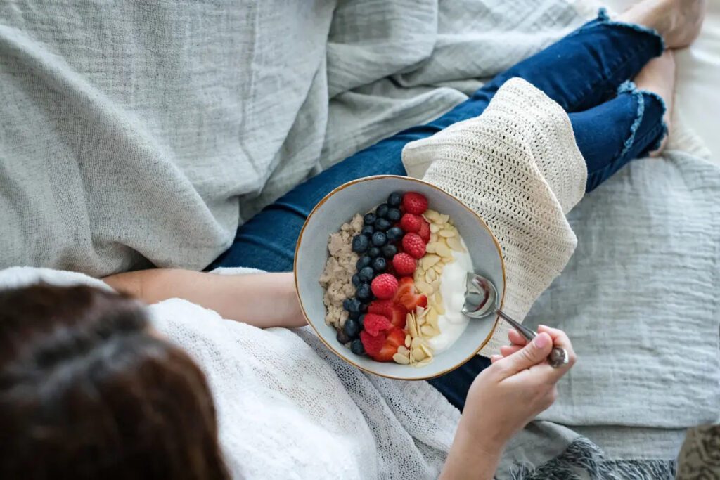 Woman Eating Healthy Breakfast with Blueberries Raspberries, Almonds & Cream