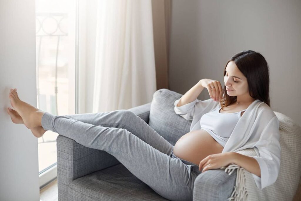 pregnant woman sitting on a comfy gray chair looking down smiling at her belly