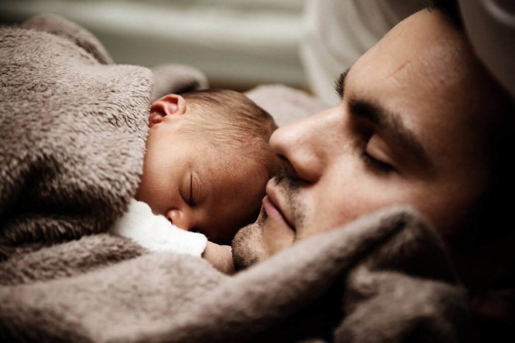 photo of father comfortably laying down with his baby