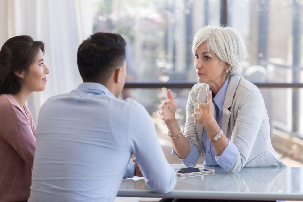Confident senior Caucasian female marriage counselor gestures while giving advice to young couple.