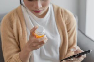 Asian woman Search for information on Internet in smartphone with holding bottled drug. girl reading information online on mobile phoneÂ medicine healthcare product concept