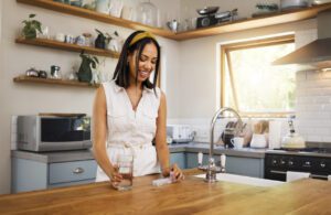 Woman drink medicine pills with a glass of water or supplement capsule in her kitchen apartment. Latino female in recovery with a pill or medical prescription drug for health, wellness or energy