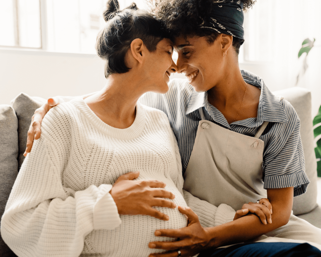 A loving lesbian couple shares an intimate moment, embracing a pregnant belly. The image symbolizes family, parenthood, and LGBTQ+ love.