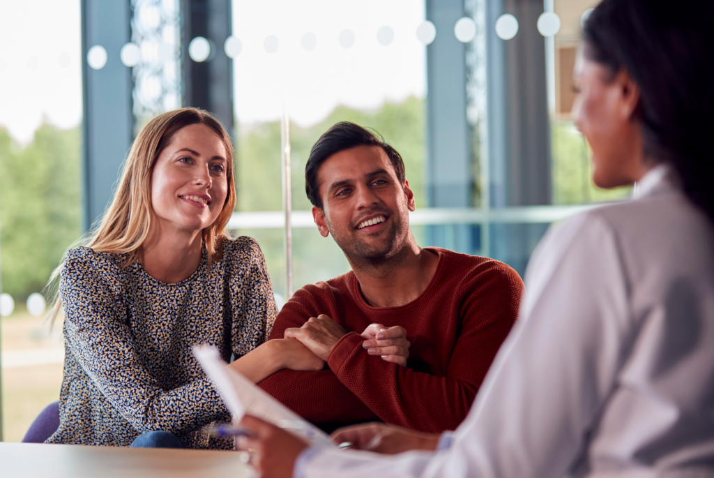 A hopeful couple smiles while meeting with a fertility specialist, discussing their journey and treatment options in a supportive setting.