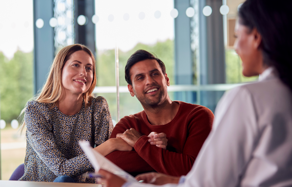 A hopeful couple smiles while consulting a fertility specialist, symbolizing expert guidance and support on their path to parenthood.