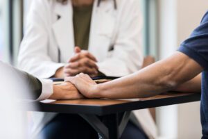 Couple holds hands as doctor with clasped hands gives news