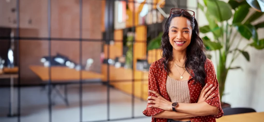 A confident woman smiles with arms crossed in a modern office, possibly reflecting on her fertility journey or planning for the future.