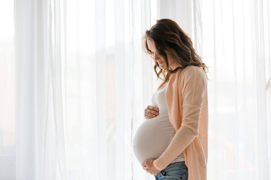 A serene and intimate moment capturing a pregnant woman cradling her belly, bathed in soft natural light.