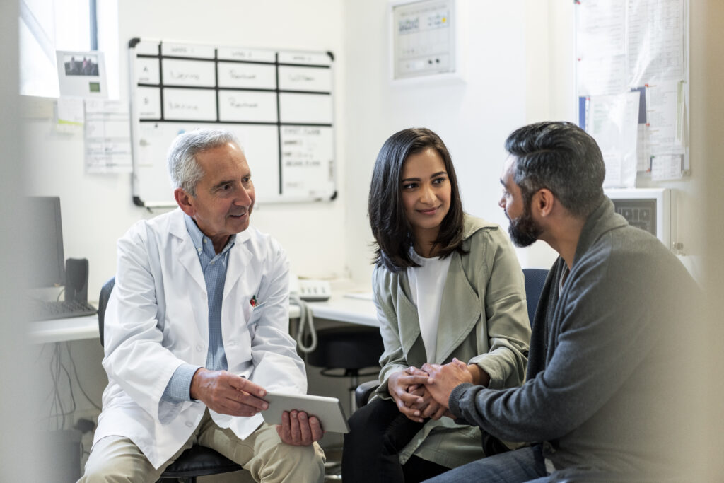 A couple holds hands while consulting with a fertility specialist, discussing their treatment options in a supportive and caring environment.