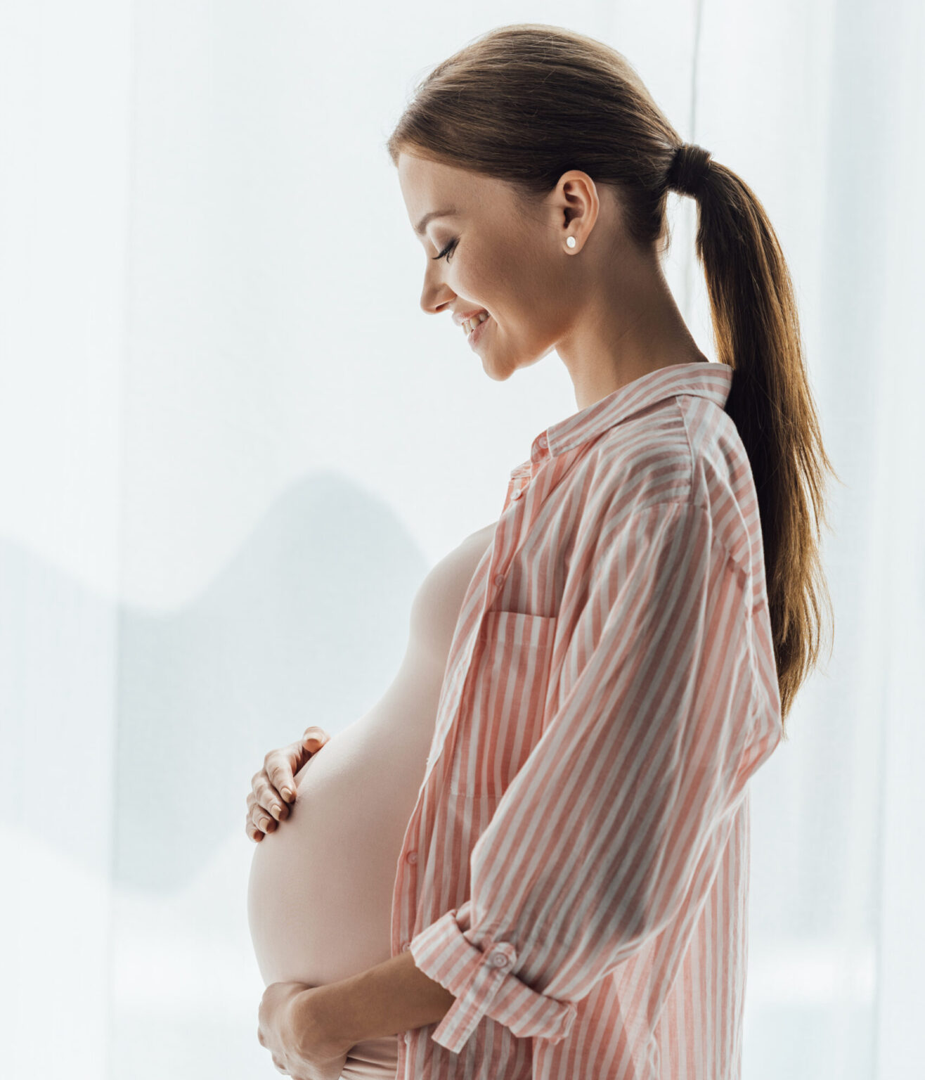 Pregnant woman in a striped shirt smiles while gently holding her belly.