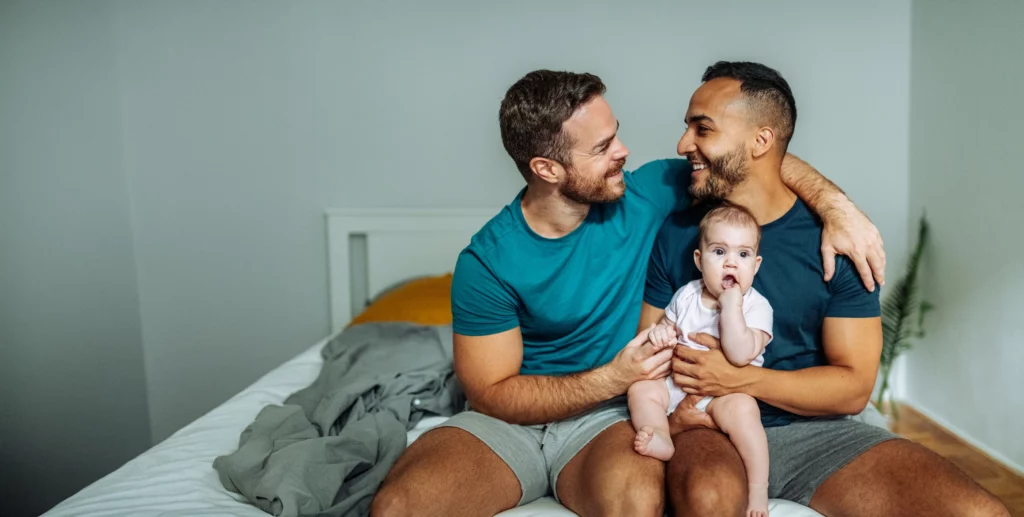 A beautiful moment of love and family, as two fathers share a joyful embrace while holding their baby.