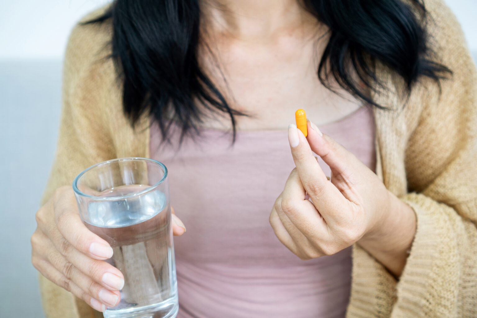 A woman holds a fertility supplement and a glass of water, preparing to take a prenatal vitamin or medication to support reproductive health.