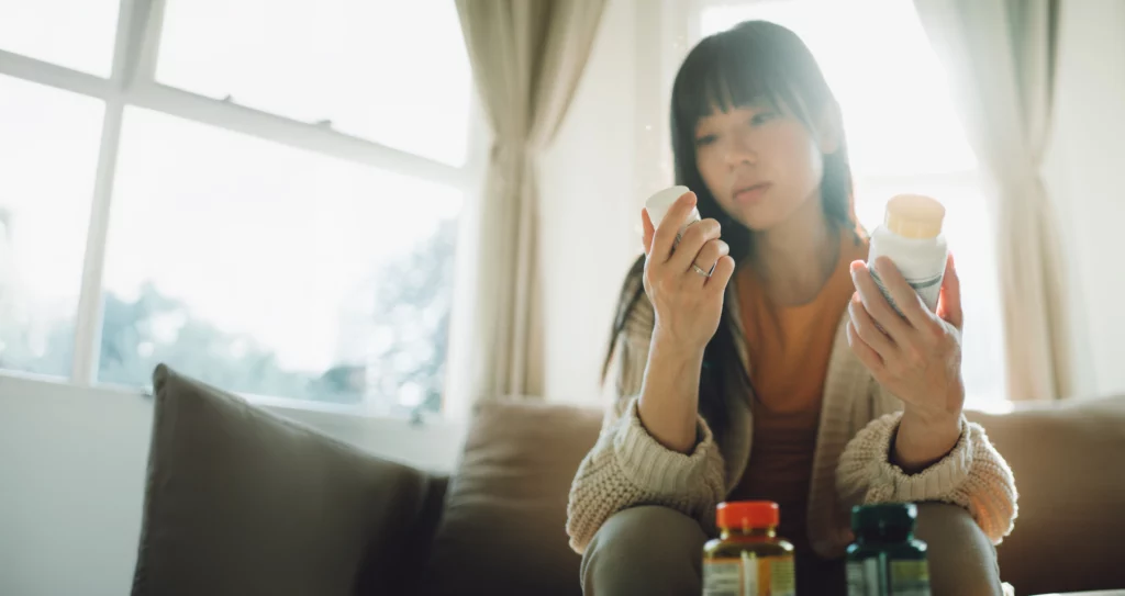 A woman sits on a couch, thoughtfully examining supplement bottles, possibly considering fertility vitamins or prenatal care options.