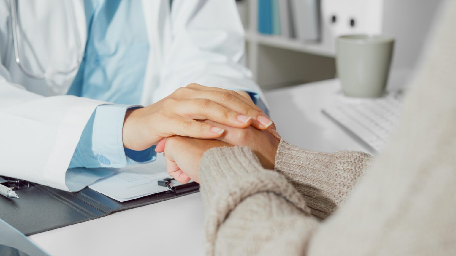 A doctor holds a patient's hands in a reassuring gesture, symbolizing compassionate care and support during a fertility consultation.