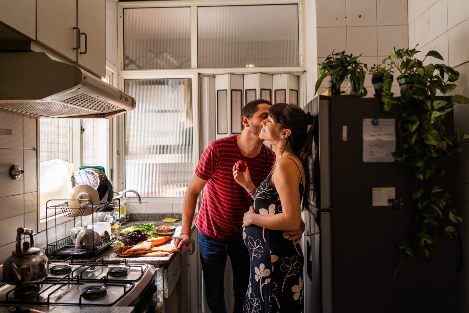 A joyful couple shares a loving moment in the kitchen, as the expecting mother cradles her belly, symbolizing the excitement of pregnancy.