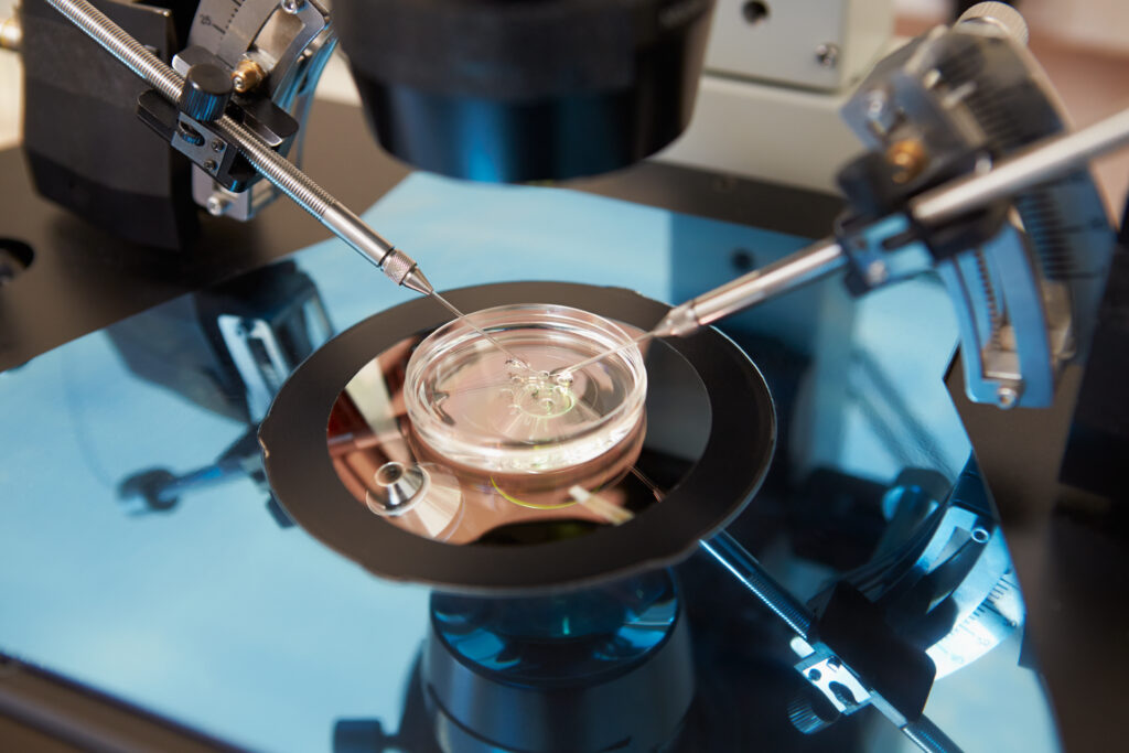 A close-up of an IVF procedure shows a microscope and precision tools injecting sperm into an egg, representing advanced fertility treatments.