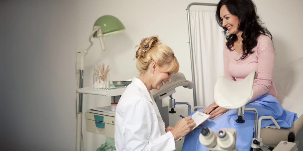 A woman smiles as she consults with her doctor in a comfortable and professional medical setting, discussing reproductive health and wellness with confidence.