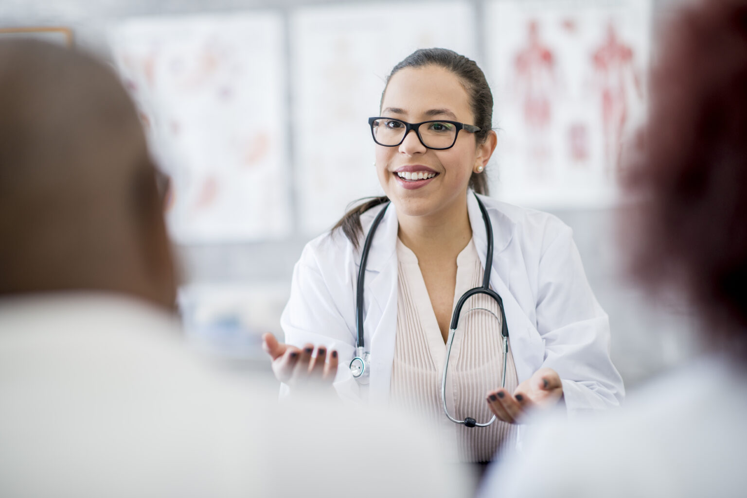 Female doctor with a stethoscope smiles and speaks to two patients.