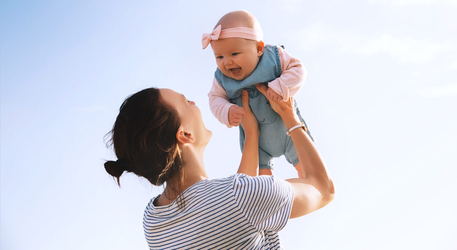 Young mother throws up baby in the sky, summer outdoors.