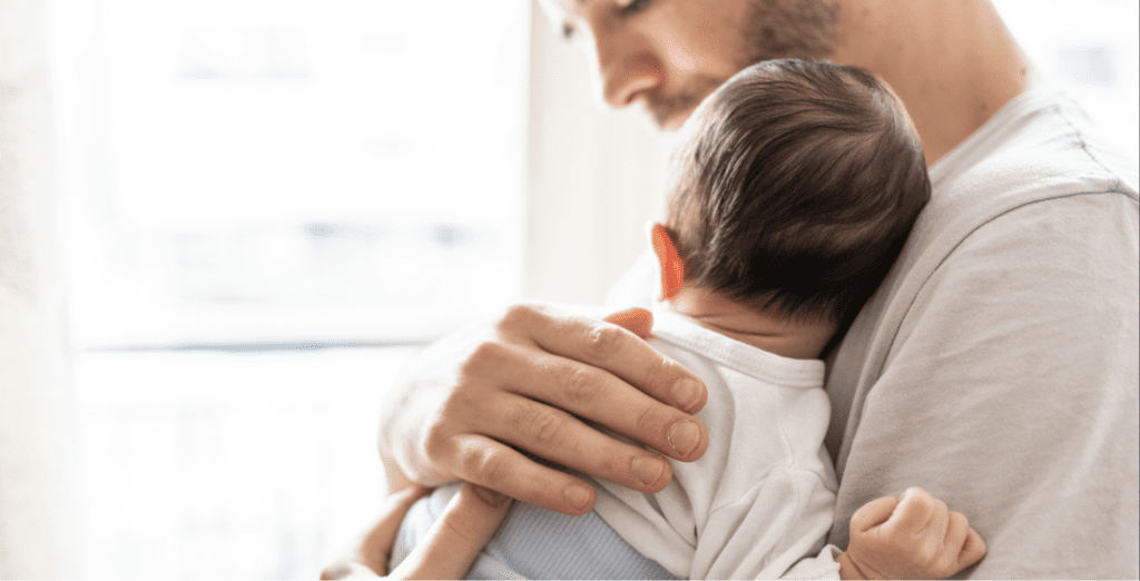 father looking down in comfort holding baby close to chest