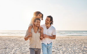 Gay couple, piggyback and relax with family at beach for seaside holiday, support and travel mockup. Summer, vacation and love with men and child in nature for lgbtq, happiness and bonding together