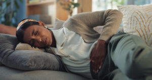 Girl, pain and hands on stomach on couch for menstruation, abdominal ache and pelvic congestion syndrome or miscarriage. Woman, home and ovarian cysts or endometriosis and gastrointestinal disorder.